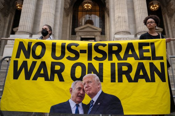 Dos activistas sostienen una pancarta grande amarilla que dice "No US-Iran war on Iran" (no a la guerra de US e Israel en Iran) junto a las fotos de Trump y Netanyahu en la fachada de un edificio imponente.